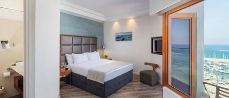 A hotel room with a bed, bedside table, and a view of the sea through a large window.