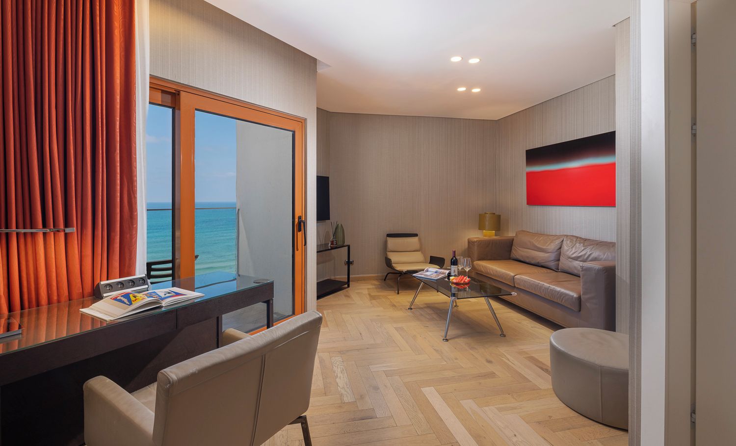 Una habitación de hotel moderna con suelo de madera, una mesa de vidrio, un sofá y vista al mar.