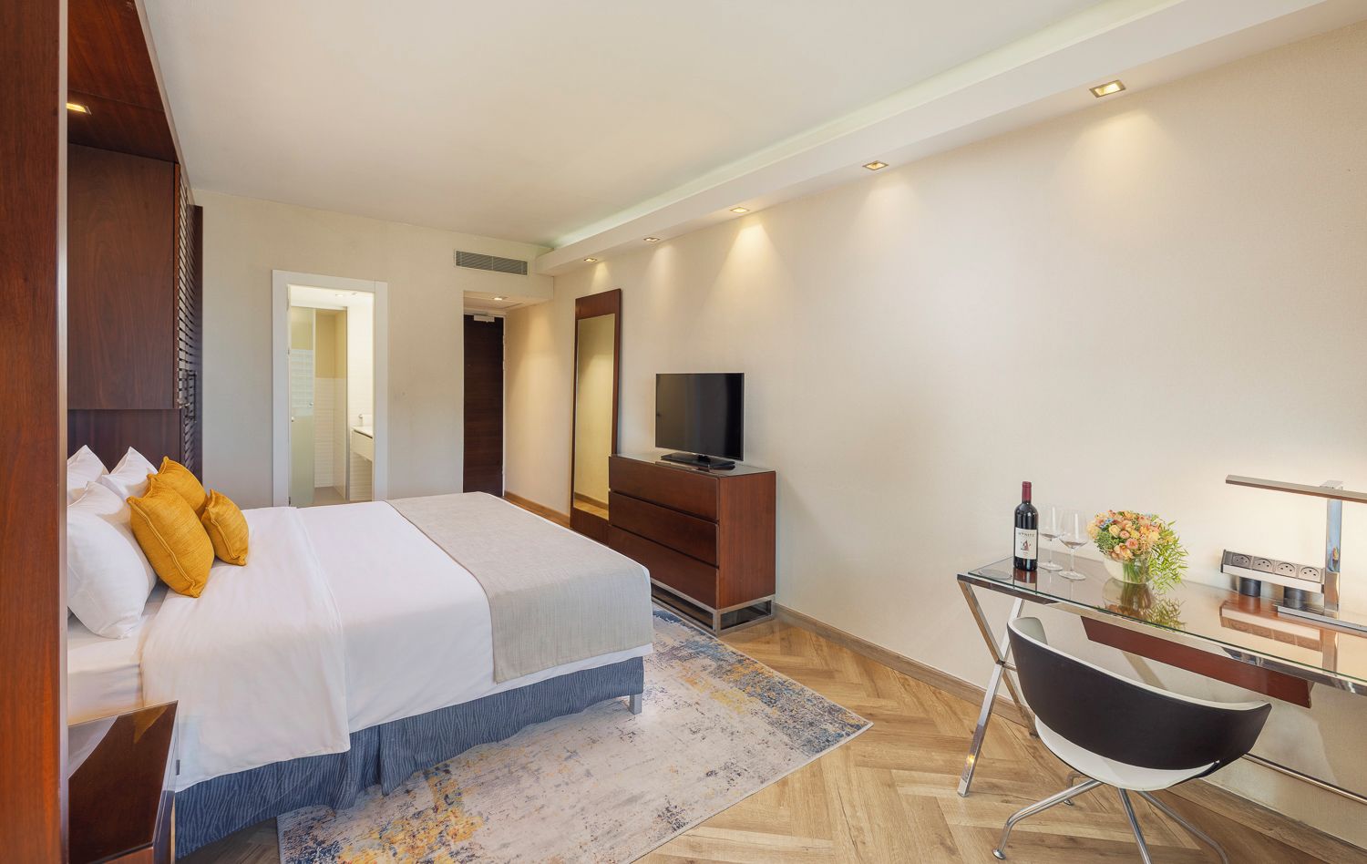 Una habitación de hotel moderna con una cama grande, un escritorio con silla, televisor y minibar.