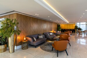 Eine moderne Lobby mit einer Couch, Sesseln, einem Couchtisch und einer großen Pflanze.