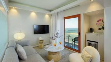 Habitación de hotel moderna con sofá, una mesita redonda, televisor de pantalla plana, balcón con vista al mar y una kitchenette.