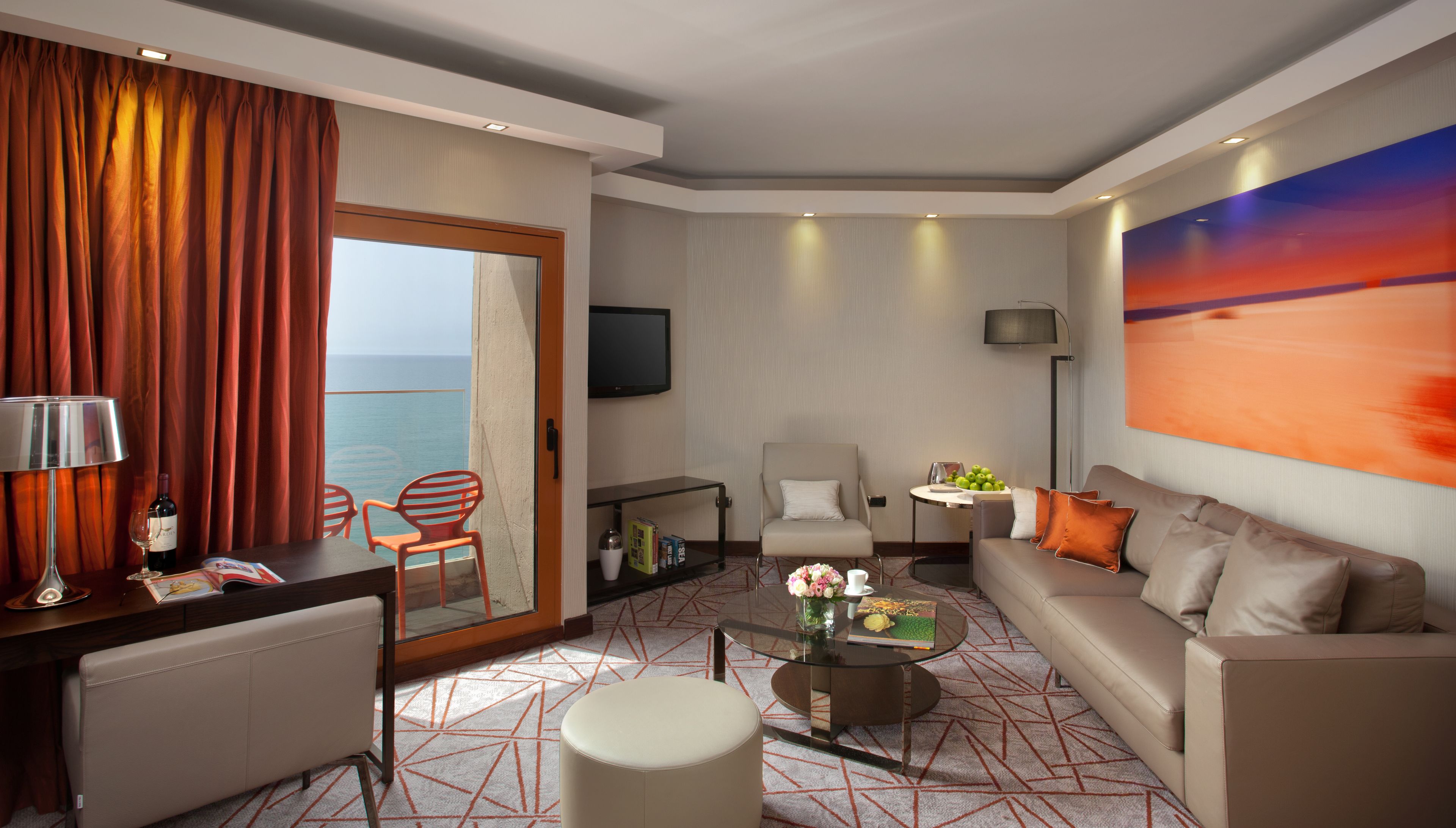 A modern hotel room with a balcony, a sofa, a dining table, and a TV.