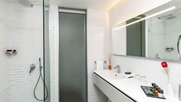 A modern bathroom with a glass shower enclosure, a white vanity with a mirror, and a red rose on the counter.