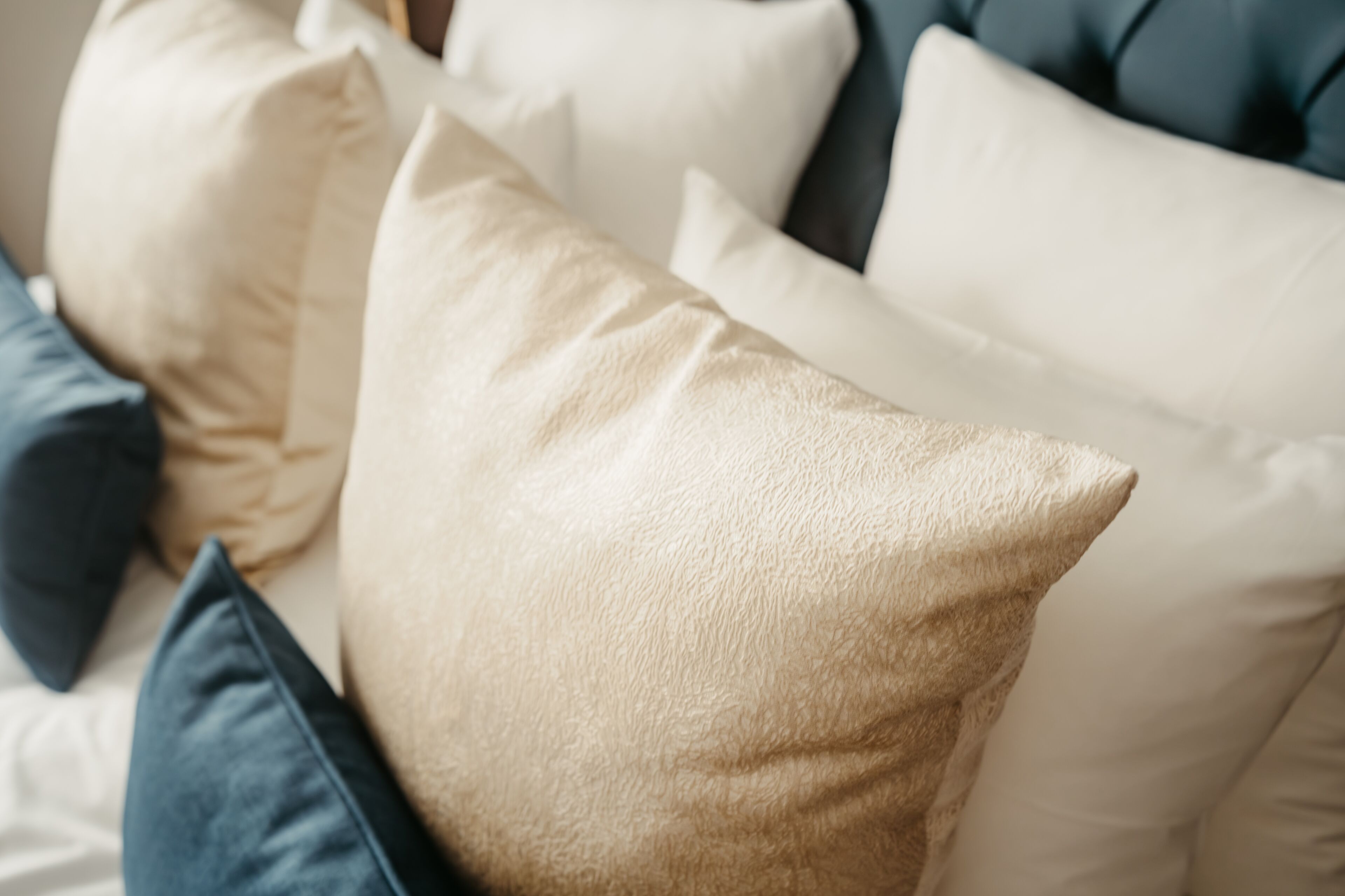Primer plano de una cama con varios almohadones en tonos beige y azul.