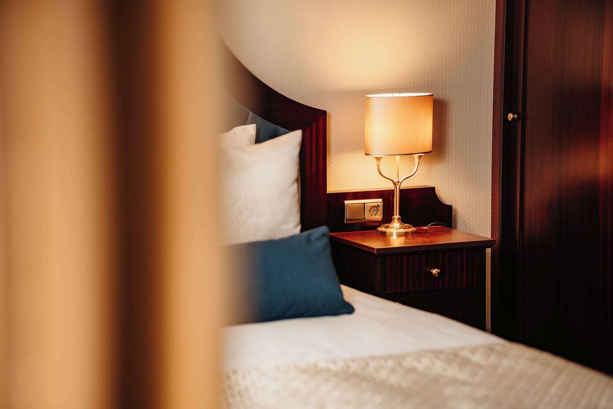 A hotel room with a neatly made bed, a bedside lamp, and a wooden nightstand.