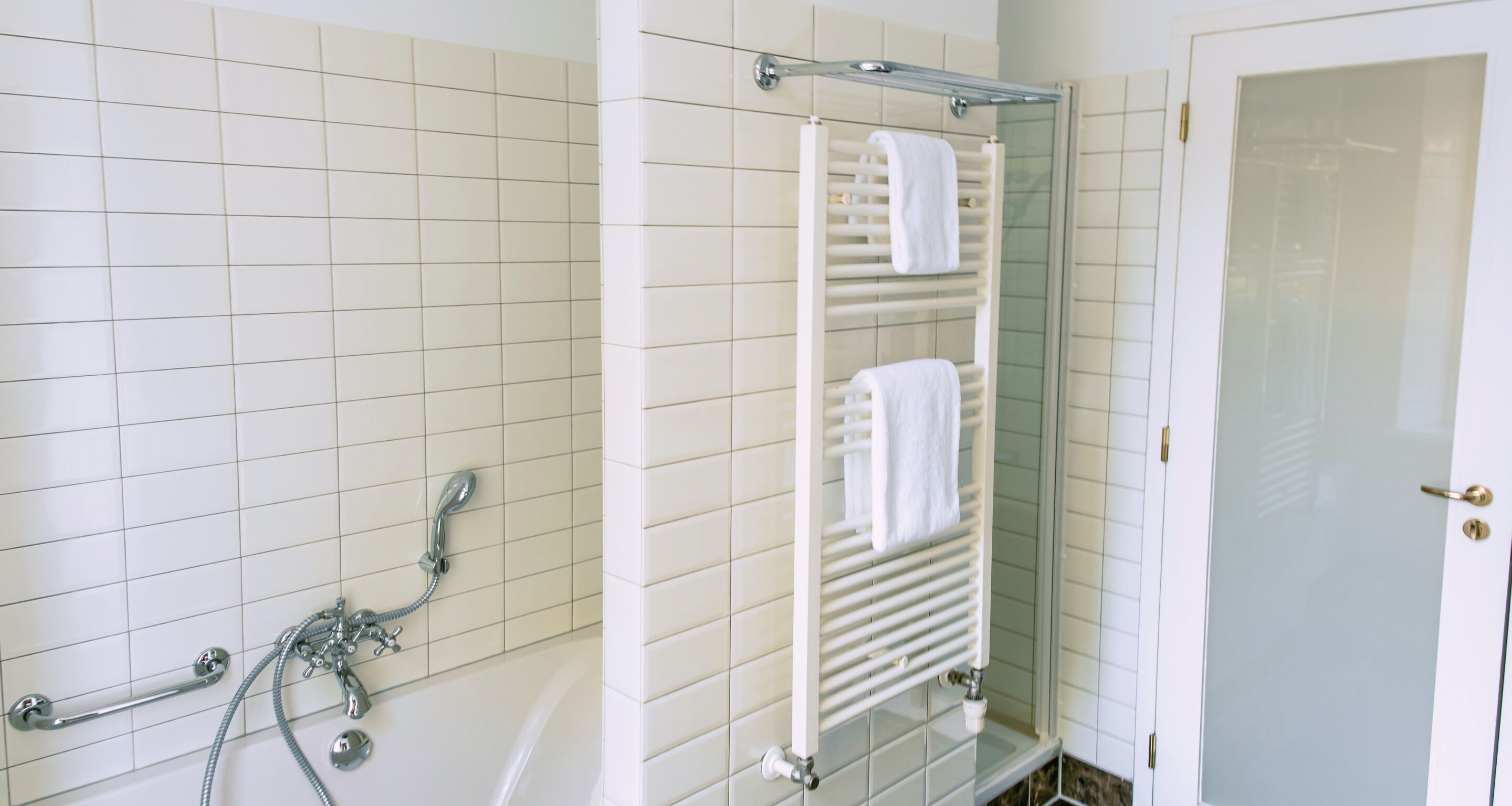A bathroom with a bathtub, a glass shower enclosure, and a towel rack with two towels.