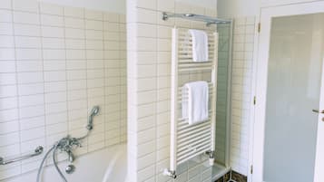 A bathroom with a bathtub, a glass shower enclosure, and a towel rack with two towels.