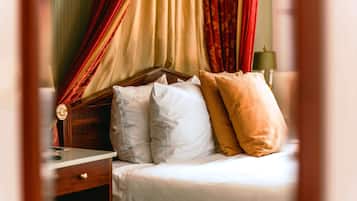 A neatly made bed with white and mustard pillows, a wooden headboard, and red curtains.