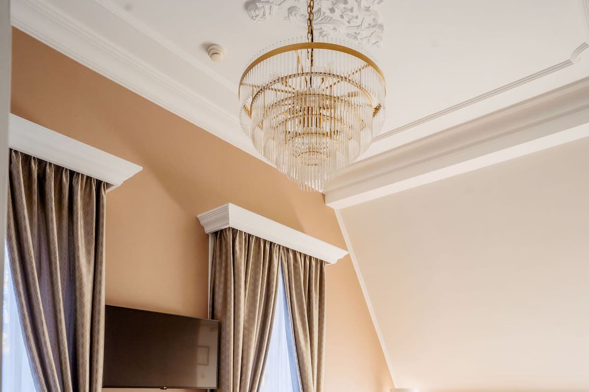 A hotel room with a large bed, a chandelier, a dining table with chairs, and a TV mounted on the wall.