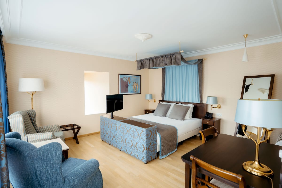 A hotel room with a bed, a desk, a chair, a sofa, and a TV.