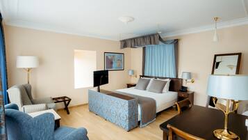 A hotel room with a bed, a desk, a chair, a sofa, and a TV.
