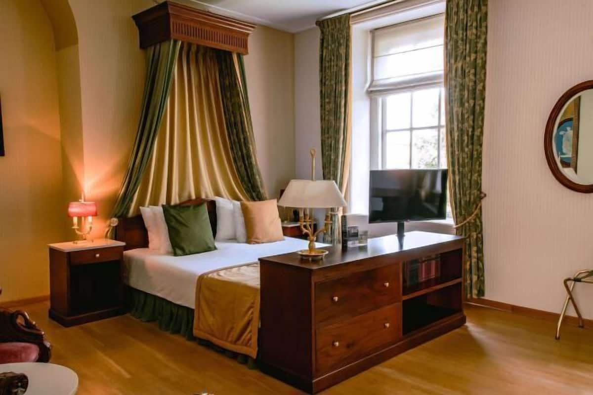 A bedroom with a canopy bed, bedside tables, a dresser, a television, and a window with curtains.
