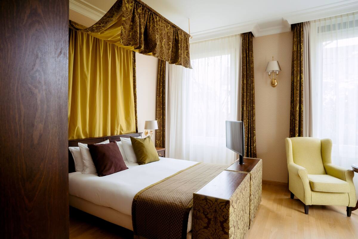 A hotel room with a large bed, a bedside table, a chair, and a television.