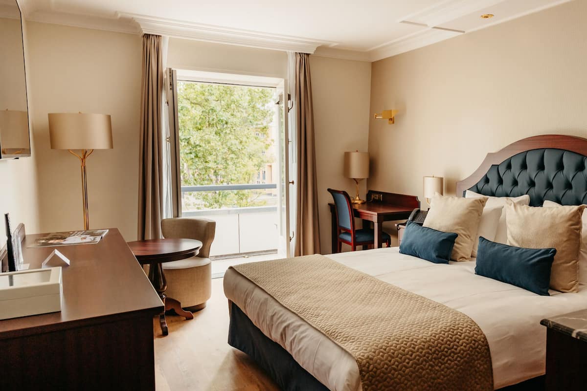 A hotel room with a large bed, a desk, a chair, and a window with curtains.