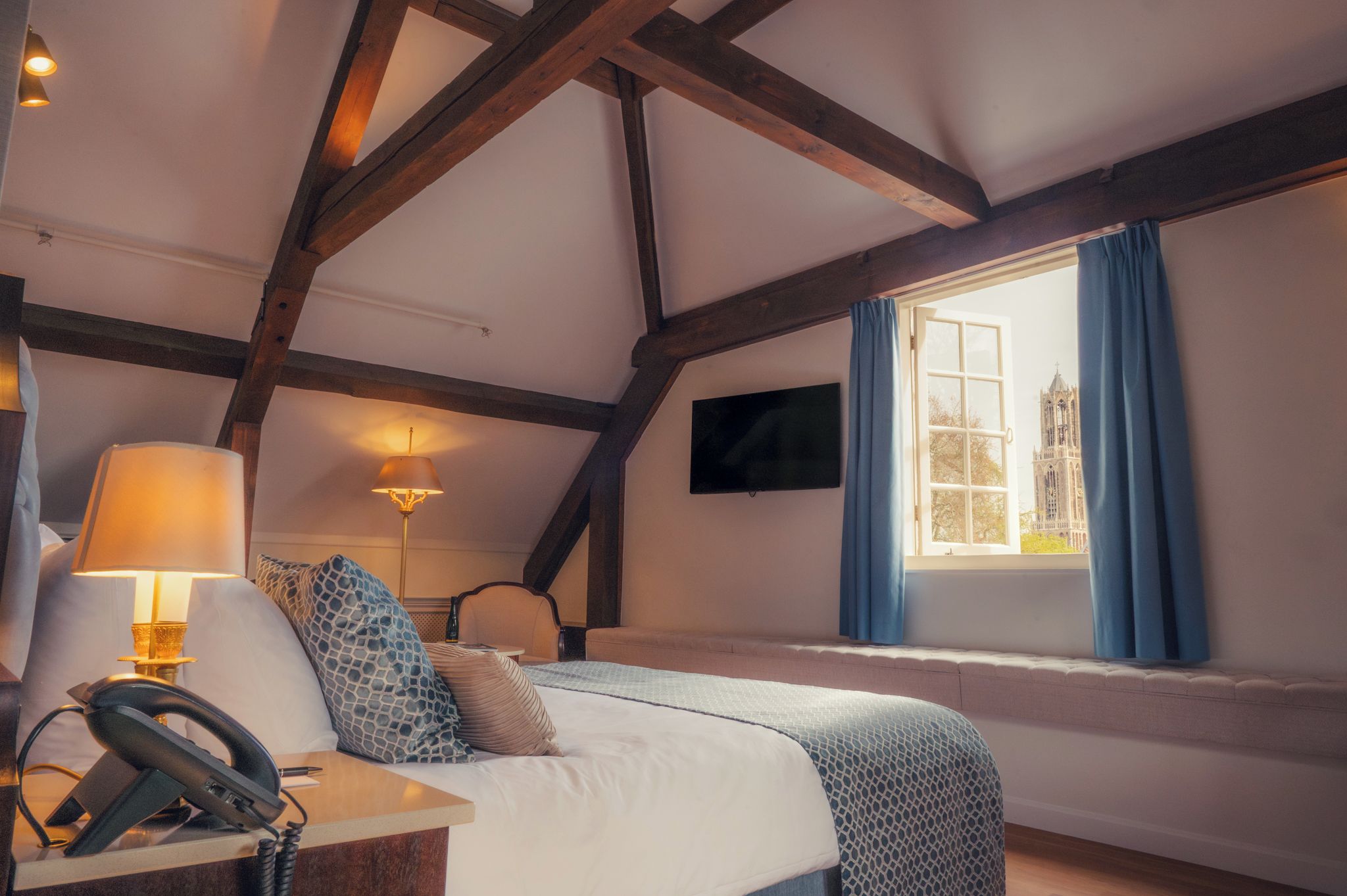 A bedroom with a bed, bedside lamps, a flat-screen TV, and a window with curtains.