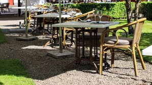 Un área de comedor al aire libre con mesas y sillas, cubierta por sombrillas y rodeada de follaje.