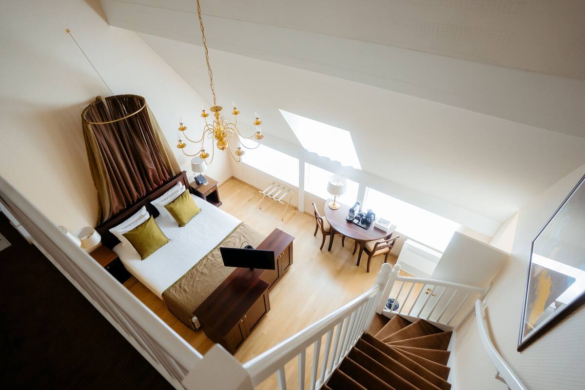 A high-ceilinged room with a bed, a dining table, and a staircase.
