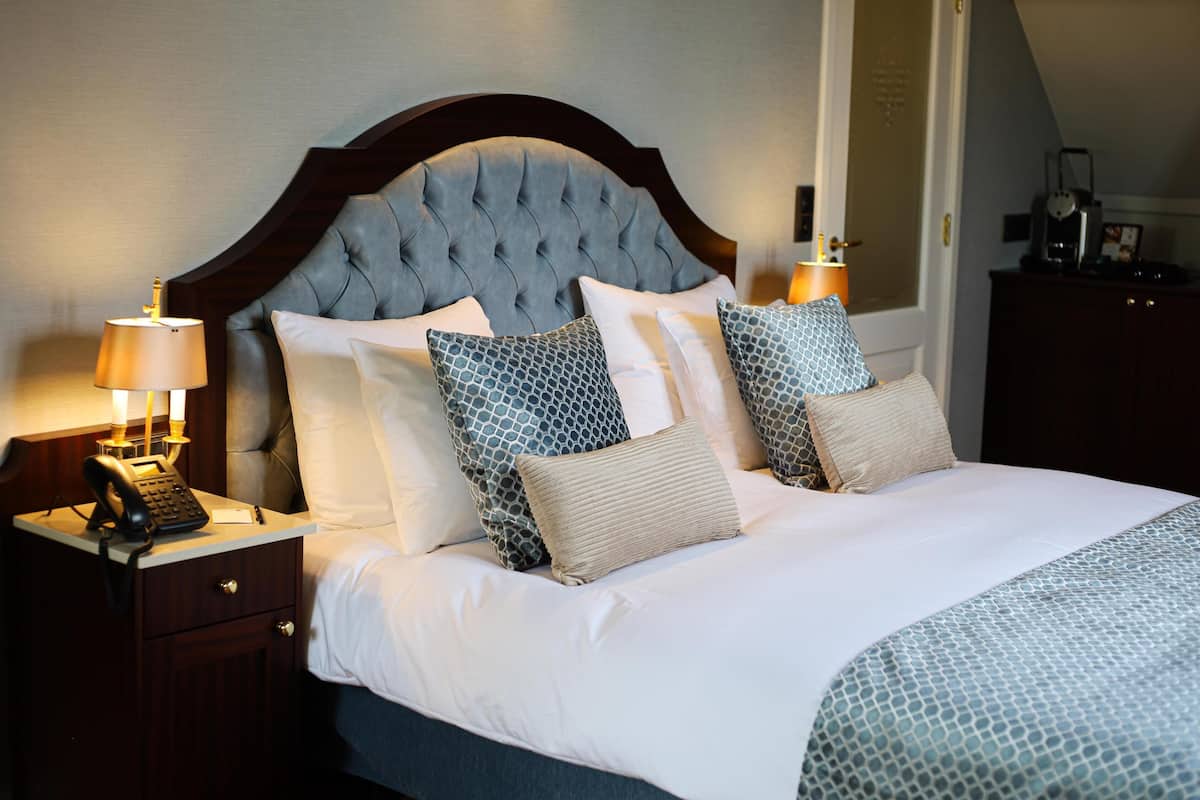 A neatly made bed with a tufted headboard, multiple pillows, and a bedside lamp.
