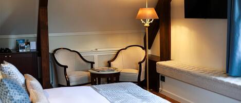 Habitación de hotel con una cama, dos sillones, una mesita, una lámpara, un televisor y un banco.