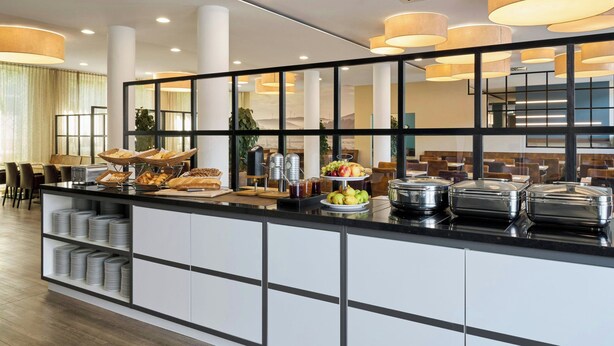 Un área de desayuno de hotel moderna con un sistema de bufé, que incluye frutas, bollería y bebidas.