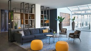 Una sala de estar moderna con un sofá azul oscuro, dos otomanas amarillas, una mesa de centro y una estantería con plantas.
