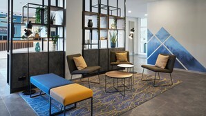 Un área de descanso moderna con un banco azul, dos sillones, una mesita de centro y una pared decorativa con un diseño geométrico.