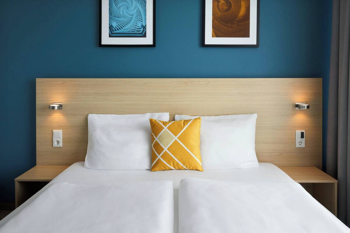 A double bed with white linens, a wooden headboard, and two bedside tables with wall-mounted lamps.