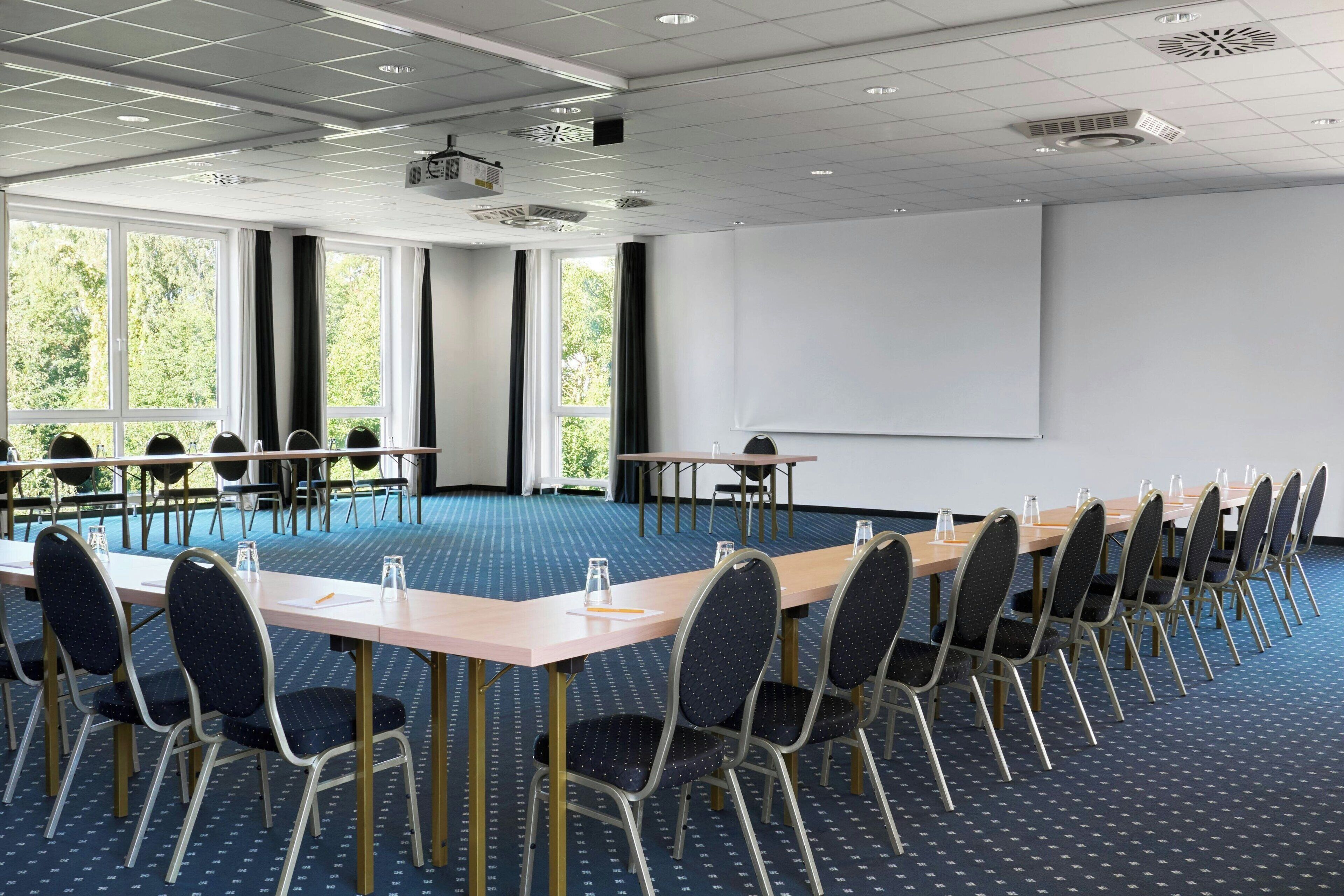 A conference room with a long table, chairs, a projector screen, and large windows.