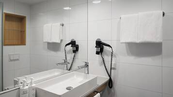 A modern bathroom with a large mirror, white sink, and two hair dryers mounted on the wall.