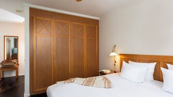 Ein Hotelzimmer mit großem Holzschrank, einem Bett mit weißer Bettwäsche, einer Nachttischlampe und einem Holz-Kopfstück.