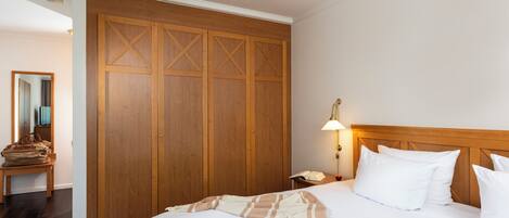 Habitación de hotel con un armario grande de madera, una cama con ropa de cama blanca, una lámpara de noche y un cabecero de madera.