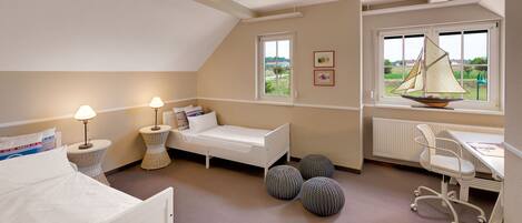 A bedroom with a bed, bedside lamp, pillows, a small round table, a chair, a radiator, and a window with a sailboat view.