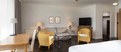 A hotel room with a bed, a desk, a chair, a sofa, a television, and a ceiling fan.