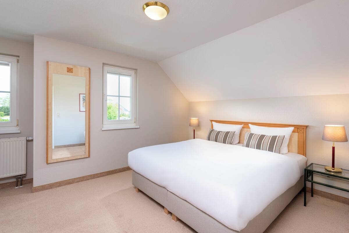 A bedroom with a large bed, two bedside lamps, a mirror, and a radiator.