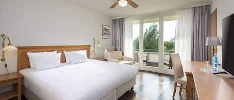 A hotel room with a large bed, a desk, a chair, a ceiling fan, and a view of the outdoors.