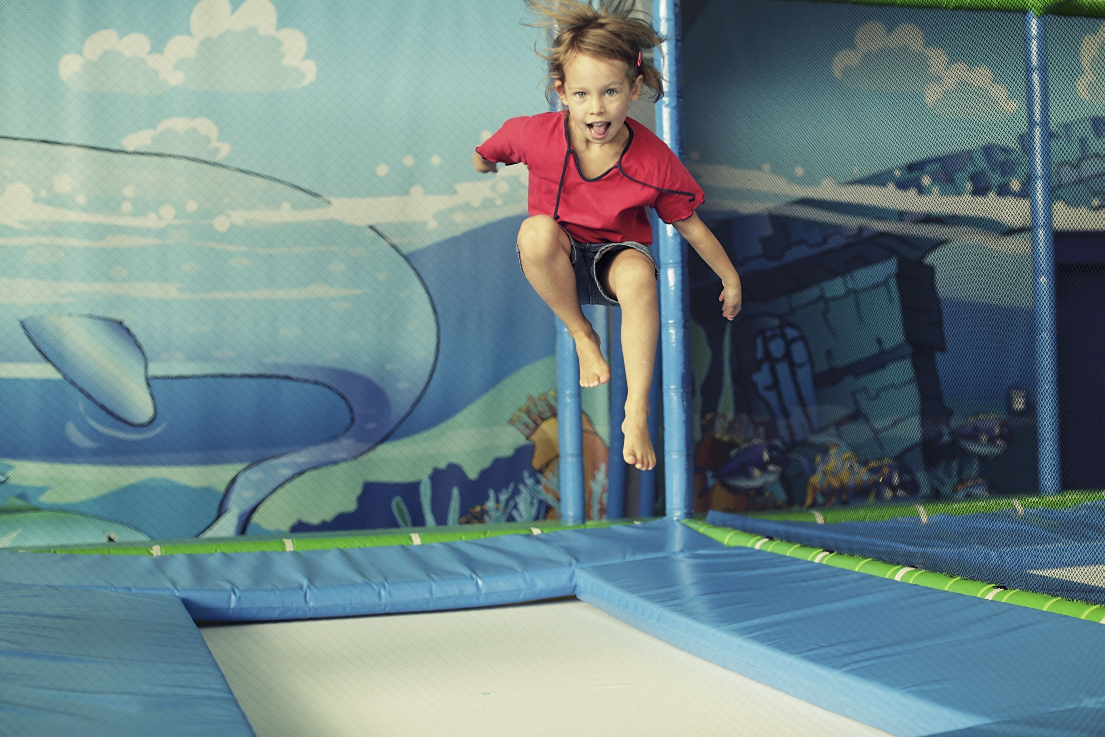 A child jumping on a trampoline with a blue and green play area, including a whale mural.