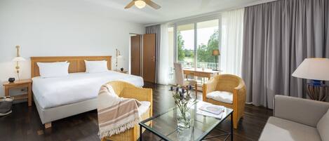 Una camera d'albergo con un letto, due poltrone in vimini, un tavolino in vetro, una scrivania e vista sull'esterno.