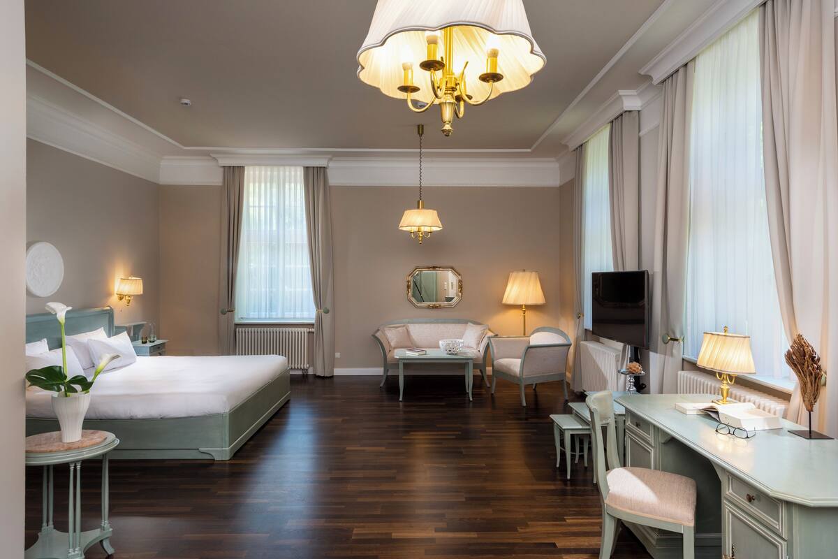 A hotel room with a bed, a desk, a chair, a sofa, and a television.