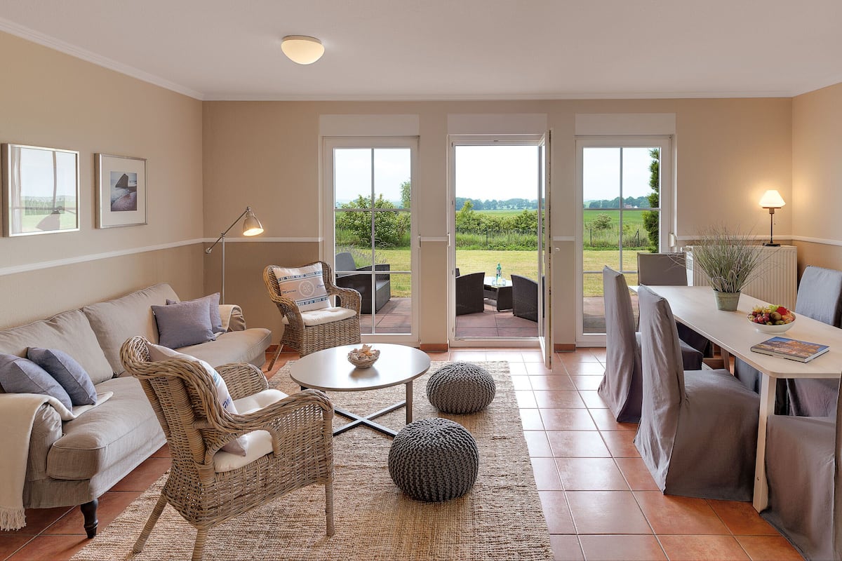 A spacious living area with a sofa, chairs, a dining table, and a view through large glass doors to an outdoor garden.