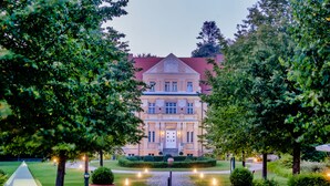 A grand building with a symmetrical facade, a central entrance, and a well-maintained garden with pathways and lighting. - Sunday Resort Rügen (Sagard)