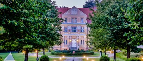 A grand building with a symmetrical facade, a central entrance, and a well-maintained garden with pathways and lighting.