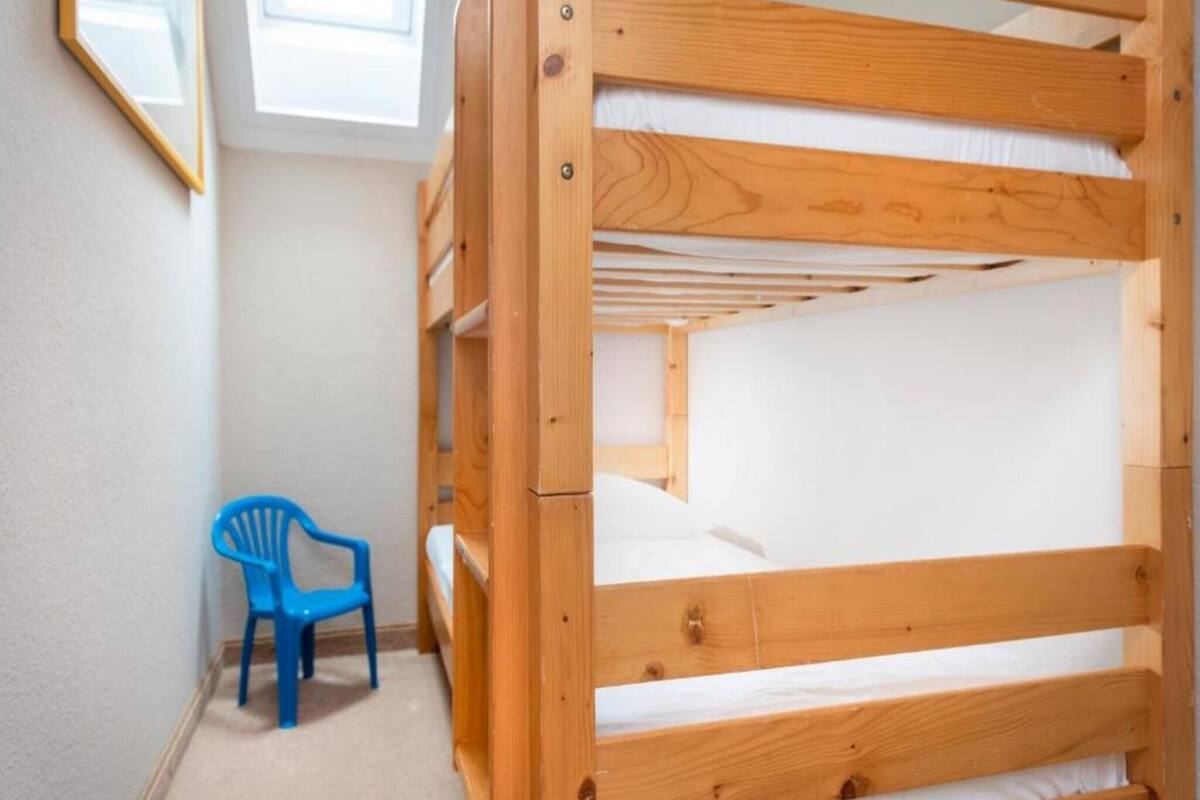 A bunk bed with a blue chair in a room with white walls and a window.