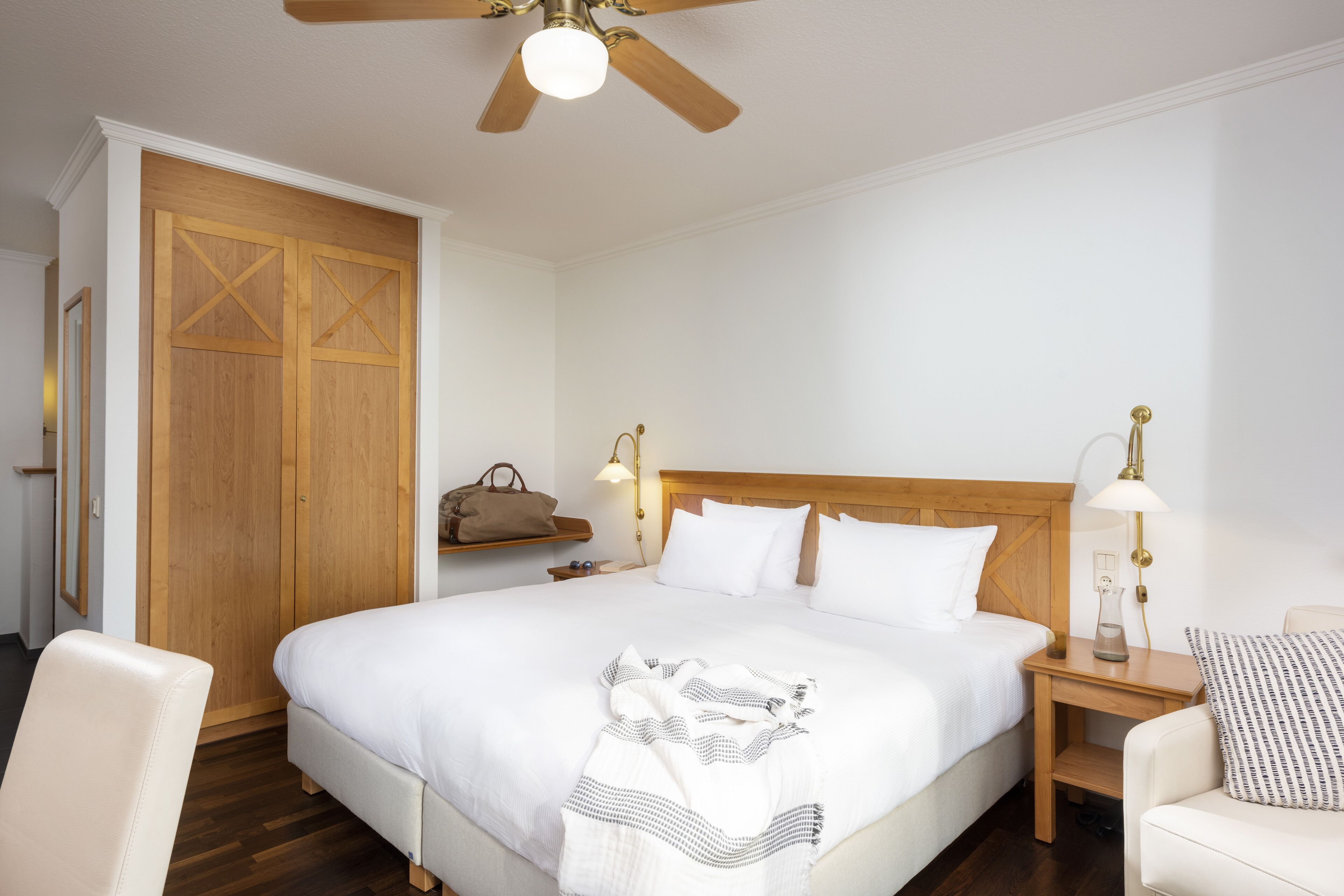 Ein Hotelzimmer mit einem großen Bett, einem hölzernen Kopfteil, zwei Nachttischen mit Lampen, einem Deckenventilator und einem Schrank mit Holztür.