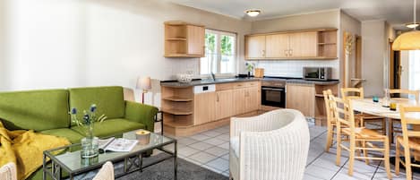 A compact living space with a kitchenette, a green sofa, wicker chairs, and a dining table.