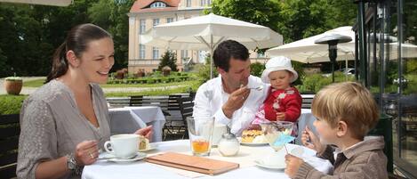 A group of people dining at an outdoor table with a view of a large building in the background.