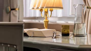 A desk with a lamp, a book, a glass pitcher, and a pair of glasses.