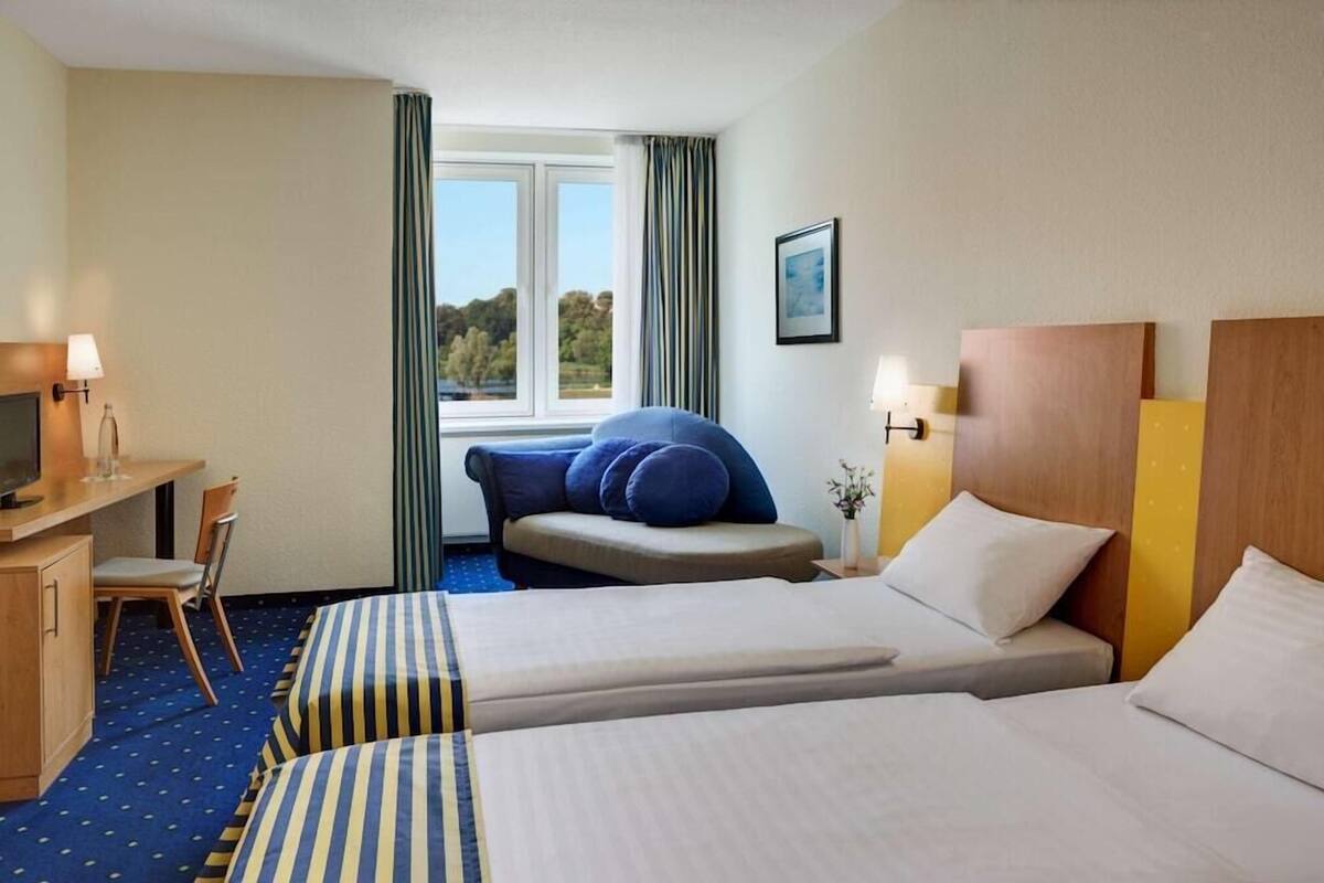 A hotel room with two beds, a desk with a chair, a television, and a window with curtains.