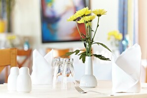 A dining table set with white tableware, a clear glass salt and pepper set, and a vase with yellow flowers.