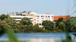 A hotel with multiple floors, surrounded by lush greenery and a body of water. - IntercityHotel Stralsund (Stralsund)