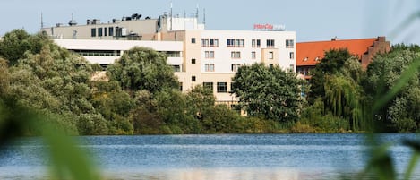 A hotel with multiple floors, surrounded by lush greenery and a body of water.